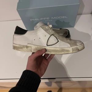 Philippe model  - Snygga vita sneakers från Philippe Model med svarta detaljer och snörning. Skorna har en klassisk design med en smutsig look på sulan för en trendig stil. Perfekta för en avslappnad och stilren look. Köpte skorna för 3900 kr! Skorna är i nytt skick så ungnifär 9/10  Dom har inga defekter.Tyvärr inget kvitto. Hör gärna av er vid funderingar! /// sweclothes örebro 