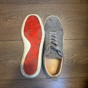 Grå sneakers från Christian Louboutin - Snygga grå sneakers från Christian Louboutin med den ikoniska röda sulan. Skorna har snörning och är tillverkade i ett stilrent material som ger en lyxig känsla. Perfekta för den som vill ha en touch av elegans i vardagen. andvända 3 gånger