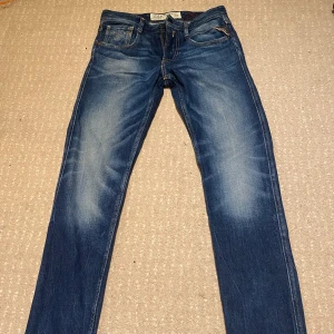 Blå Replay Anbass - Snygga blå jeansbyxor från Replay och diskreta slitningar för en trendig look. Storlek W29 L32. Byxorna har en knappgylf och är perfekta för en avslappnad stil. Modellen är Anbass. Vid frågor och funderingar är det bara att säga till!