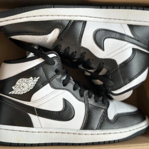 Nike Air Jordans i svart och vitt - Snygga Nike Air Jordans i klassisk svart och vit färgkombination. Skorna har en hög design med snörning och den ikoniska Air Jordan-loggan på sidan. Perfekta för dig som vill ha en stilren och sportig look.