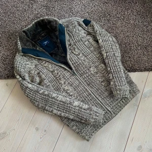 Fodrad Cardigan Stickad - Säljer denna snygga grå/beiga fodrade cardigan i storlek M. Perfekt för att hålla värmen och samtidigt vara riktigt stilig. Perfekt skick, inga defekter!