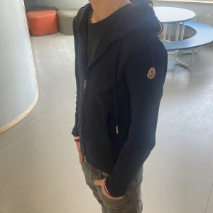 Mörkblå huvtröja från Moncler - Säljer en snygg mörkblå huvtröja från Moncler med dragkedja och huva. Tröjan har långa ärmar och Moncler-logga på ärmen. Perfekt för en stilren look. Den är knappt använd bara 2 gånger pris kan ändras vid snabb affär