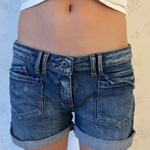 Lågmidjade Blå jeansshorts med upprullade ben - Snygga blå jeansshorts med upprullade ben och klassisk femficksdesign. Shortsen har en knapp- och dragkedjestängning samt bälteshällor för extra stil. Perfekta för en avslappnad look. Kolla gärna in mina andra shorts💕