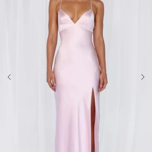 Ljusrosa långklänning med slits - Helt ny, superfin ljusrosa långklänning i satin med smala axelband och djup slits framtill. Klänningen har en öppen rygg med snörning. Perfekt till speciella tillfällen som exempelvis bal.