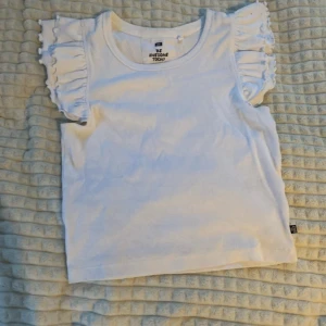 Vit topp med volangärmar från WE - Säljer en söt vit topp från WE med volangdetaljer på ärmarna. Toppen är ärmlös och har en rund halsringning.