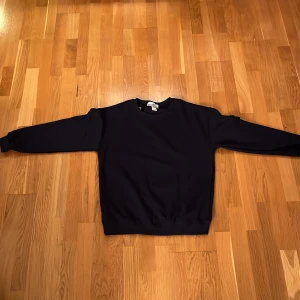 Mörkblå sweatshirt från Stone Island - Säljer en stilren mörkblå sweatshirt från Stone Island. Tröjan har långa ärmar och ett ikoniskt märke på ärmen. Perfekt för en casual look. Den passar folk mellan 175-182 cm.
