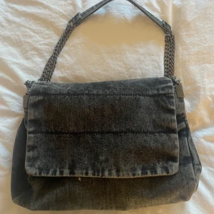 Grå axelväska i jeansmaterial - Snygg grå axelväska i jeansmaterial med kedjedetaljer på axelremmen från zara. Väskan har en bra storlek om man vill få plats med det mesta man behöver, i väskan finns det även två innefack där det rymmer gått om plats, skriv för fler bilder💕