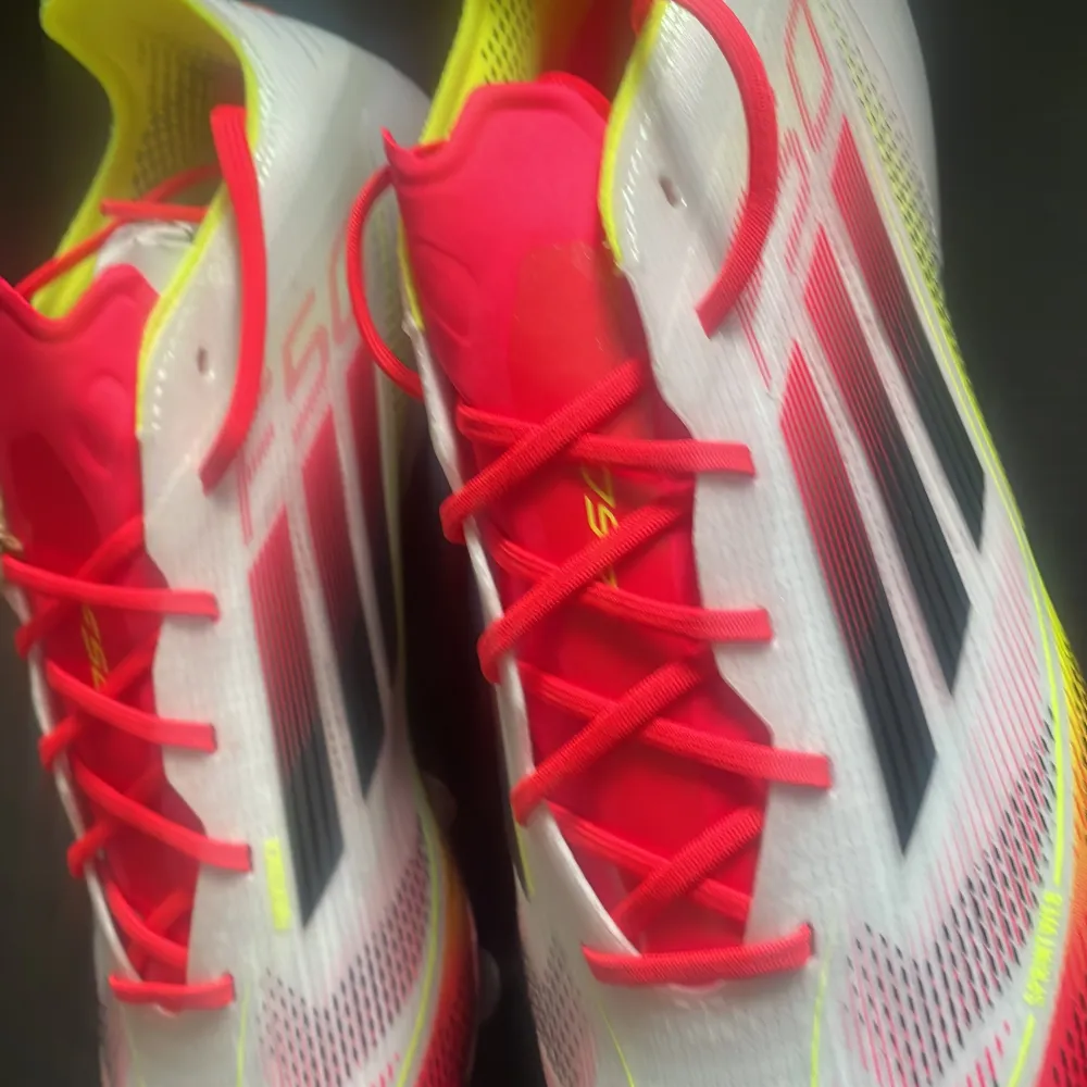 Snygga Adidas fotbollsskor i vitt med neonrosa och neongula detaljer. Skorna har snörning och en modern design som passar perfekt för fotbollsplanen. Helt nya . Kengät.