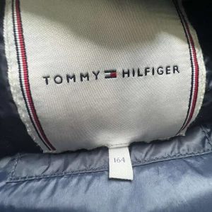 Mörkblå pufferjacka från Tommy Hilfiger - Säljer en svart pufferjacka från Tommy Hilfiger i storlek xs 164. Jackan har en quiltad design med dragkedja framtill och två sidofickor. 