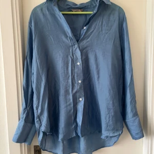 Blå skjorta från H&M - Snygg blå skjorta från H&M i en mjuk och lätt materialblandning av lyocell och polyamid. Skjortan har en klassisk krage och knappar. Lite skir. 