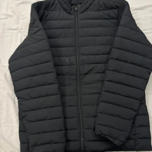 Svart pufferjacka - Säljer en stilren svart pufferjacka med dragkedja. Jackan har långa ärmar och är perfekt för kyligare väder. Den quiltade designen ger extra värme och komfort. Detta är en jack and Jones jacka som har ett ordinarie pris på 600kr, men jag säljer den för 350kr. Priset kan diskuteras om det är så att ni vill. Använd minst 6 gånger och är i ett jätte bra skick.