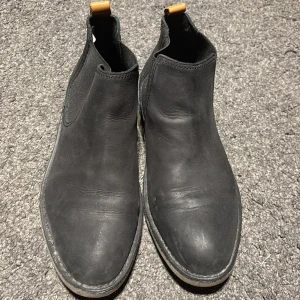Svarta Chelsea boots - Snygga svarta Chelsea boots från Bianco med elastiska paneler och dragflik i orange. Perfekta för en stilren look.