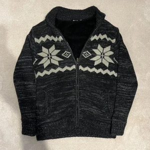 Fodrad Cardigan  - Mysig svart stickad kofta med dragkedja och ett stilrent mönster i vitt. Perfekt för kyliga dagar med sin varma insida. Koftan har långa ärmar och ribbade muddar för extra komfort. Vid minsta fråga eller fundering hör av er🤝