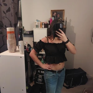 Svart offshoulder topp - Trendig svart offshoulder topp med volangdetaljer och croppad passform. Perfekt för en stilren look.