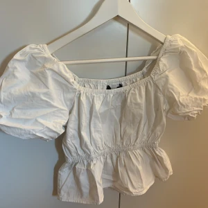 Vit blus med puffärmar - Säljer en söt vit blus med puffiga kortärmar och elastisk midja. Perfekt för en somrig look med sin luftiga design och volangdetaljer. Passar bra till både jeans och kjol.