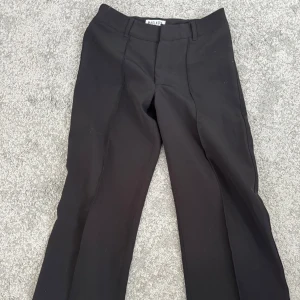 Svarta kostymbyxor från Madlady - Snygga svarta kostymbyxor från Madlady med en klassisk design. Byxorna har en rak passform och är perfekta för en stilren look. De har hällor för bälte och en diskret dragkedja framtill. Byxorna är lågmidjade och i storlek xs/s