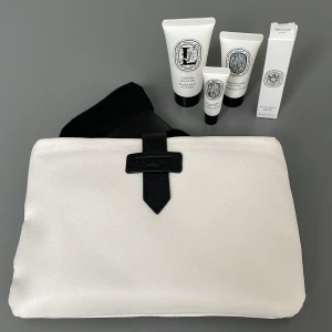 Set med parfymer och hudvård från Diptyque - Exklusivt set från Diptyque med en eau de toilette, kroppslotion, ansiktskräm och läppbalsam. Kommer i en stilren vit necessär med svart läderdetalj och mönstrad insida. Perfekt för resan eller som en lyxig present.