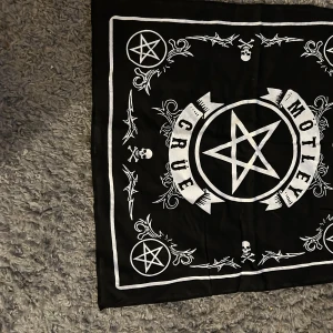 Svart bandana med Mötley Crüe-motiv - Cool svart bandana med Mötley Crüe-design. Den har vita detaljer med pentagram och dödskallar, perfekt för rockfans. Bandanan är fyrkantig och kan användas som accessoar eller dekoration.