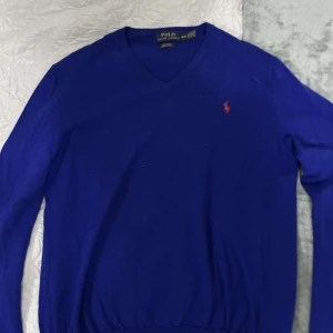 Blå tröja från Polo Ralph Lauren - Snygg blå tröja från Polo Ralph Lauren i merinoull. Tröjan är en v-ringad. STORELK M. Perfekt för en stilren look.