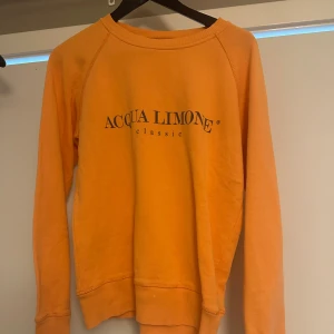 Orange tröja från Acqua Limone - Säljer en snygg orange tröja från Acqua Limone med tryck både fram och bak. Tröjan har långa ärmar och ribbade muddar vid ärmslut och nederkant. Perfekt för en avslappnad stil. Älskar färgen och speciellt på sommaren när man vill se lite extra brun ut❤️