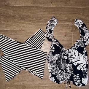 Två toppar i randigt och blommigt mönster - Säljer två snygga toppar. Den ena är en svartvit randig offshoulder-topp och den andra är en svart blommig topp med knytning framtill. 