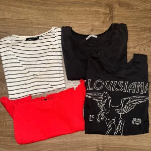 Fyra olika t-shirts i varierande stilar - Säljer ett set med fyra t-shirts: en vit och svart randig. En vanlig mörkgrå, en hallonröd offshoulder och en T-shirt med louisiana tryck 