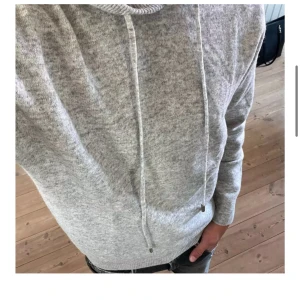 Grå Merinoull hoodie - Säljer en stilren grå hoodie med justerbar huva och långa ärmar. Perfekt för en avslappnad look. Den är mjuk och bekväm, idealisk för kyligare dagar.