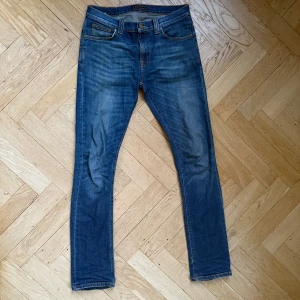 Blå Nudie Jeans - Snygga blå jeans från Nudie Jeans med en klassisk femficksdesign och knappgylf. Passformen är slim och modellen heter TUBE TOM. Jeansen är i bra skicka förutom att högra backfickan har lite slitage. Nypris 2700kr mitt pris 399kr. Skriv vid frågor och funderingar!