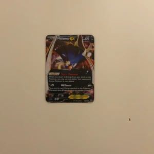 Pokémonkort Malamar EX - Säljer ett Pokémonkort med Malamar EX. Kortet har en färgglad design med Malamar i fokus och texten 'MAXamar' och 'Hyper Hypnosis'. Baksidan har den klassiska blå Pokémon-designen med en Pokéball i mitten.