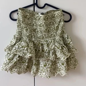 Zara kjol - Helt slutsåld minikjol från Zara med blommigt mönster i grönt och vitt. Kjolen har en volangdetalj och en elastisk midja för bekväm passform. Perfekt för sommaren, säljer då jag har för många kjolar💕