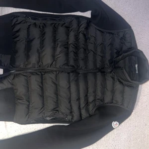Svart quiltad jacka från Moncler - Snygg svart quiltad jacka från Moncler med dragkedja och långa ärmar. Perfekt för kyligare dagar med sin stilrena design och bekväma passform.