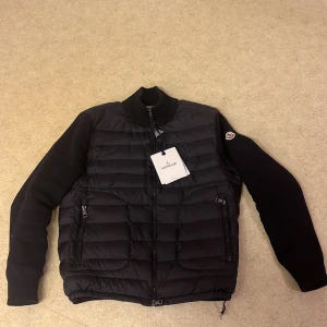 Svart quiltad jacka från Moncler - Snygg svart quiltad jacka från Moncler med dragkedja och långärmade ärmar. Jackan har en stilren design med märkets logga på ärmen. Perfekt för kyligare dagar.