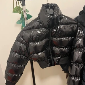 Svart pufferjacka - Snygg svart pufferjacka med hög krage och dragkedja. Perfekt för kyliga dagar med sin quiltade design som håller värmen. Jackan har en croppad passform som ger en modern look.