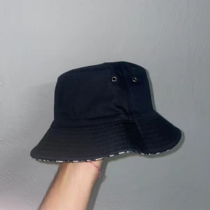 Christian Dior svart bucket hat - Snygg svart bucket hat från Christian Dior med ett unikt mönster på insidan. Hatten har små ventilationshål på sidorna för extra komfort. Perfekt för att ge din outfit en stilfull touch. Pris kan diskuteras vid snabb affär!!!