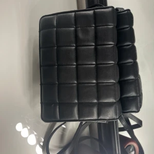 Svart quiltad axelväska - Snygg svart quiltad axelväska från Zara. Perfekt för att bära dina nödvändigheter med stil. Väskan har en praktisk dragkedja och en justerbar axelrem.