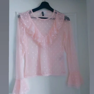Rosa blus med volangdetaljer - Söt rosa blus från H&M med volangdetaljer och prickigt mönster. Blusen har långa ärmar och en luftig passform, perfekt för vår och sommar.