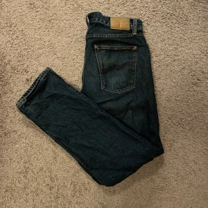 Mörkblå jeans från Nudie Jeans - Skit snygga mörkblå jeans från Nudie. Skicket är som nytt, köpta för ett halvt år sen och säljer för dem sitter lite stort. Storleken är 30/30. Modellen på jeansen heter ”gritty Jackson”. Hör av dig vid mer frågor eller bilder!