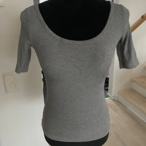 Grå ribbad topp - Snygg grå ribbad topp med trekvartsärm och rund halsringning. Perfekt för en stilren och bekväm look.