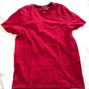 Röd herr t-shirt från Tommy Hilfiger - Snygg röd t-shirt från Tommy Hilfiger med v-ringning och korta ärmar. Perfekt för en avslappnad stil. Den har en liten logga på bröstet som ger en stilren touch.
