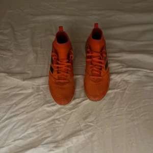 Orange fotbollsskor från Adidas - Snygga orange fotbollsskor från Adidas med svarta ränder på sidan. Skorna har snörning och är perfekta för fotboll inomhus och konstgräs. Pris kan sänkas och diskuteras 