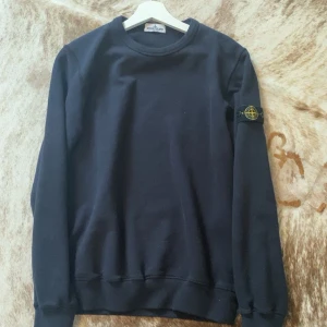  Stone Island Junior - Säljer en stilren svart tröja från Stone Island Junior. Tröjan har långa ärmar och ett ikoniskt märke på ärmen. Perfekt för en casual look.