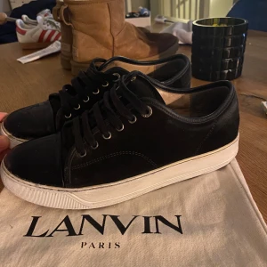 Lanvins  - Snygga svarta sneakers från Lanvin med snörning och vit sula. Skorna har en stilren design med en kombination av skinn och mocka. Perfekta för en trendig look. Skick 7,5/10. Dust bag ingår i köp, pris kan diskuteras.
