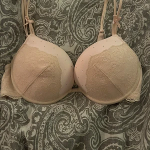 Beige spets-bh från H&M - Säljer en beige bh från H&M med spetsdetaljer och små glittriga stenar. Den har justerbara axelband med små rosetter. Inte använd mycket. 