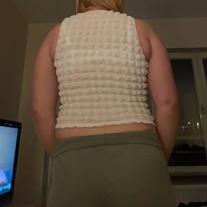 Vit ärmlös topp med knytning - Säljer en vit ärmlös topp med knytning framtill. Toppen har en ribbad struktur och är croppad, vilket ger en trendig look. Perfekt för varma dagar eller som ett lager under en jacka.