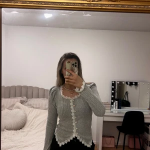 Grå ribbad kofta med spetsdetaljer - Säljer en elegant grå ribbad kofta med vackra vita spetsdetaljer längs kanterna och pärlknappar framtill. Passar xs-s🩶