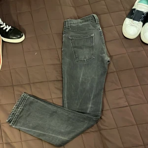 Grå jeans från Nudie Jeans - Snygga grå jeans från Nudie Jeans med en klassisk femficksdesign. De har en knappgylf och är tillverkade i ett slitstarkt denimtyg. Perfekta för en stilren look. modellen är grim tim har du frågor svara gärna så snabbt som möjligt
