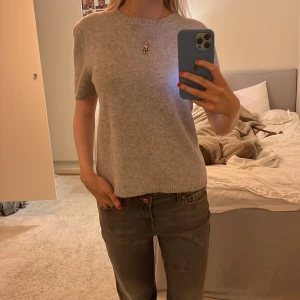 Grå kortärmad tröja - Säljer en stilren grå tröja med korta ärmar. Perfekt för en avslappnad look. Tröjan har en rund halsringning och är gjord i ett mjukt material.