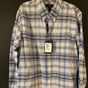 Rutig skjorta från Gant - Snygg rutig skjorta från Gant i blått och vitt. Skick 10/10, aldrig använd och lappen sitter kvar. Nypris 799, mitt pris 250. Storlek 164, men den är ganska stor så skulle säga att den passar XS.