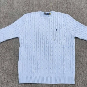 Ljusblå stickad tröja från Polo Ralph Lauren - Säljer en stilren ljusblå stickad tröja från Polo Ralph Lauren med det klassiska broderade logotypen på bröstet. Tröjan har en kabelstickad design och rund halsringning. Perfekt för kyligare dagar.