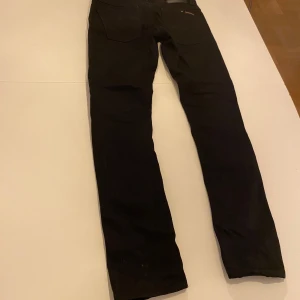 Svarta jeans från Nudie Jeans - Snygga svarta jeans från Nudie Jeans med en klassisk femficksdesign. De har en knappgylf och är tillverkade i ett slitstarkt material. Perfekta för en stilren look. Använda två gånger, nypris 1450kr 